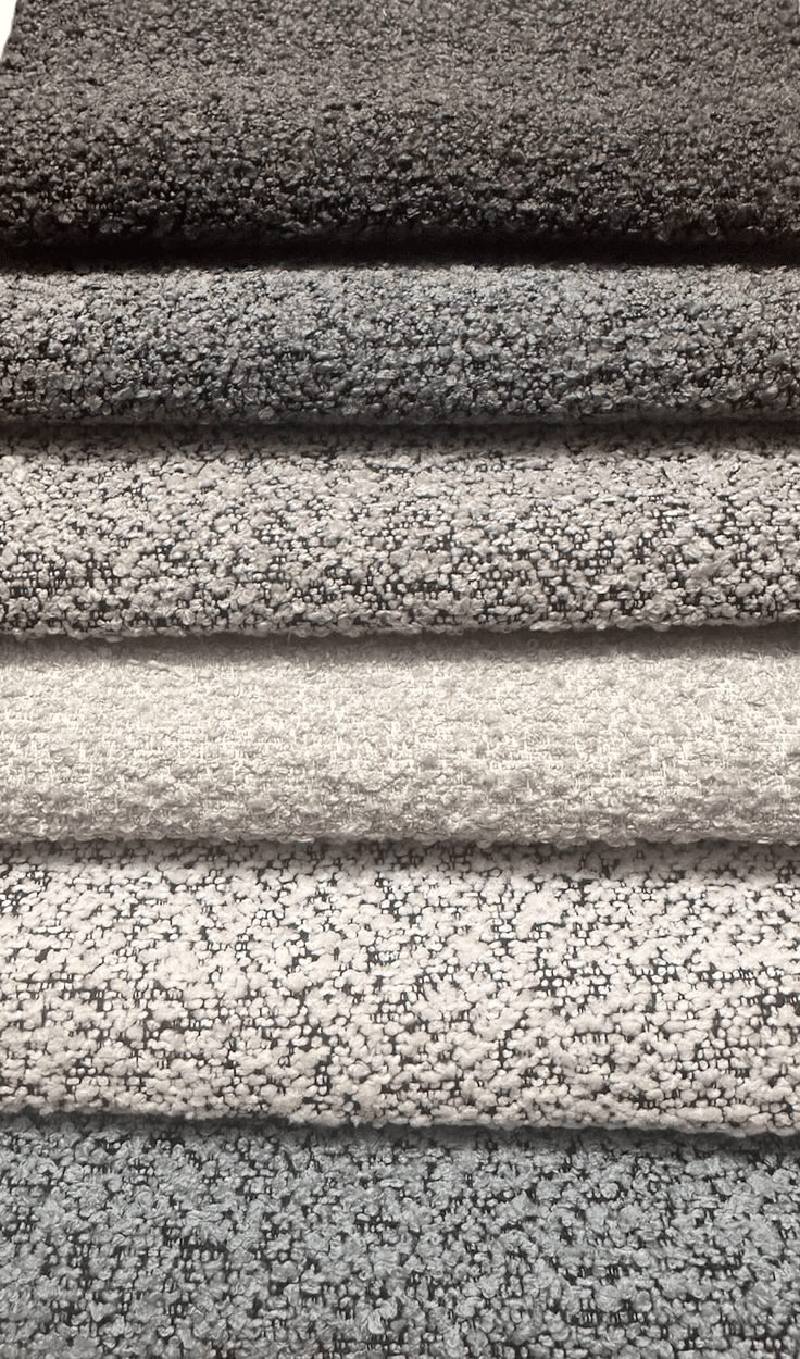 A stack of five textured fabric swatches arranged vertically. The colors range from dark gray at the top to light gray at the bottom, echoing the refined elegance of custom draperies NYC offers, showcasing a variety of shades and patterns.